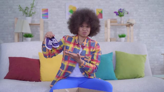 surprised and upset african american woman with an afro hairstyle unpacks the parcel,wrong size