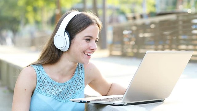 Happy woman wearing headphones using a laptop to play funny videos in a park