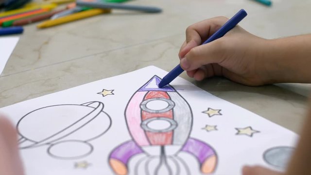 Kids coloring on a sheet of paper with crayons while sitting on the floor. Close shot of a girls hand coloring on a sheet of paper