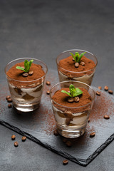 Classic tiramisu dessert in a glass on stone serving board on dark concrete background