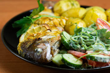Baked trout with lemon on a plate with arugula, tomato, cucumber salad and young potatoes with dill.