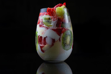 Ice cream with kiwi and strawberries in a beautiful glass cup on a black background