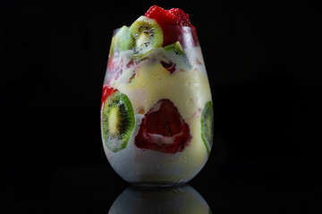 Ice cream with kiwi and strawberries in a beautiful glass cup on a black background