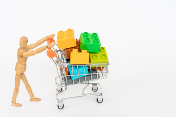 Wooden mannequin carries a shopping cart with blocks. Isolated on white