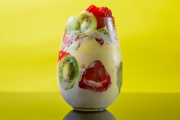 Ice cream with kiwi and strawberries in a beautiful glass cup on a yellow background