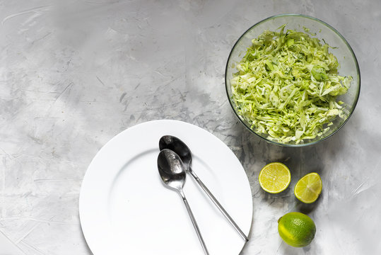 White plate with tablespoons and salad from fresh cabbage with greens