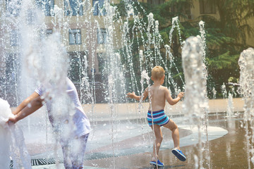 A boy playing with water in park fountain. Hot summer. Happy young boy has fun playing in water fountains