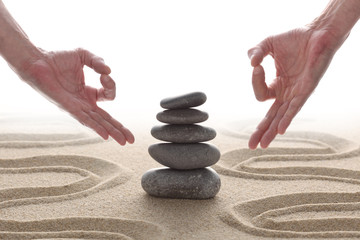 zen stones piled on raked sand with two hands in om position and copy space for your text