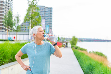 Thirsty fitness mature woman holding bottle of water. Senior sporty woman making a break from exercising. Fitness, healthcare and dieting concept