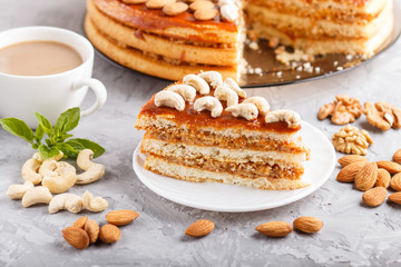 Piece of homemade cake with caramel cream and nuts with cup of coffee on a gray concrete  background, side view.