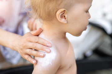 Mother applying sunscreen protection creme on cute little toddler boy shoulder. Mom using sunblocking lotion to protect baby from sun during summer sea vacation. Children healthcare at travel time