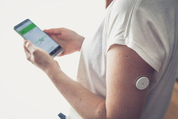 Woman checking glucose level with new technology remote sensor and mobile phone, sensor checkup glucose levels without blood. Diabetes treatment.