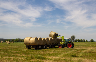 Fototapeta premium tractor loading bales of hay onto a long trailer