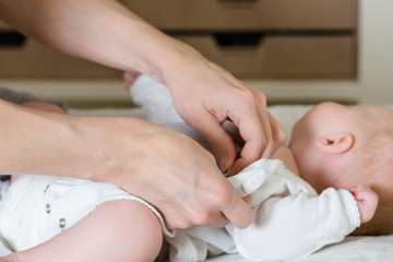 Hands of a mother who dresses her baby on a changing table.