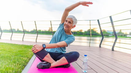 Mature woman doing yoga at park and looking away. Senior woman enjoying nature during a breathing...