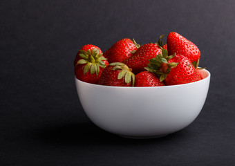 Fresh red strawberry in white bowl on black background. side view.