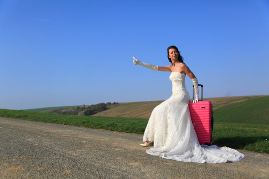 Bride hitchhiking with pink suitcase