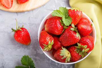Fresh red strawberry in white bowl on gray concrete background. top view.