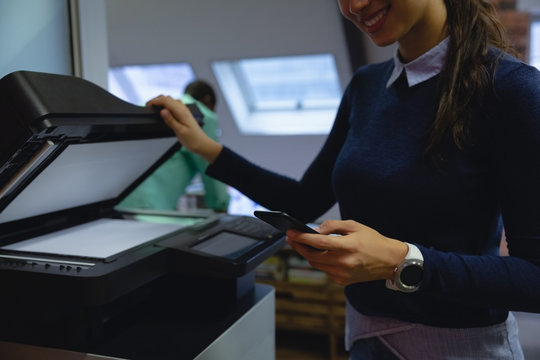 Businesswoman Using Mobile Phone While Holding Xerox Copy Machine In Hand