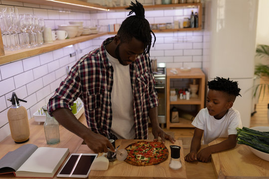  Son watching his father while cutting pizza with pizza cutter in kitchen