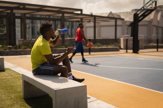 Basketball player drinking water while relaxing at basketball court 