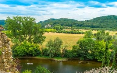 Fototapeta na wymiar Beynac-et-Cazenac, Dordogne/ France: typical landscape at Perigord with a canoe by the river Dordogne and the Castle of Castelnaud-la-Chapelle in the distance