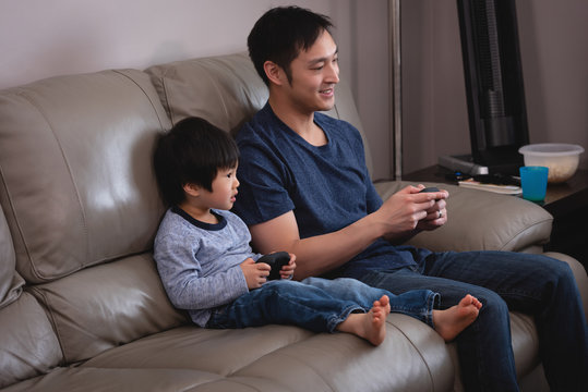 Father and son playing together video game while sitting on sofa at home