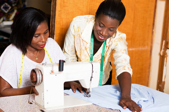 seamstress teaches her  students how to put a shirt under the needle of a sewing machine.