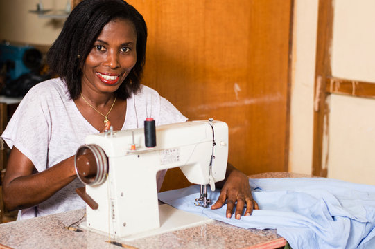 Young African woman smiling sewing in her studio in the quiet.