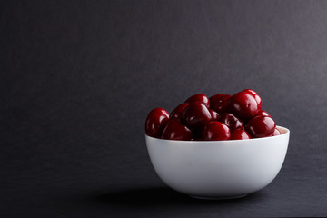 Fresh red sweet cherry in white bowl on black background. side view.
