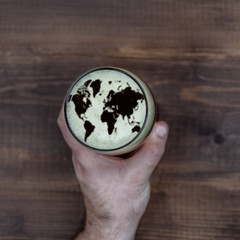 Close up man's hand holds a mug of beer with silhouettes of world map on foam