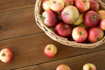 fruits, food and harvest concept - ripe apples in wicker basket on wooden table