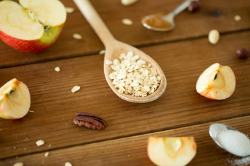food cooking and eating concept - oatmeal in spoon, cut apples and nuts on wooden table