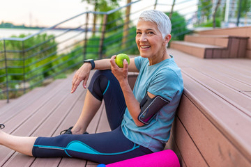 Sporty woman eating apple. Beautiful woman with gray hair in the early sixties relaxing after sport...