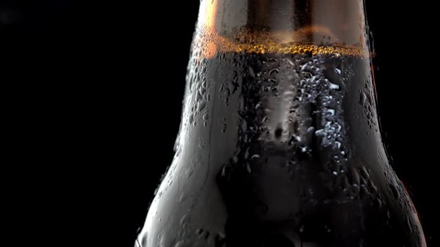 macro rotation video shooting of a bottle of cold black beer on a black background.