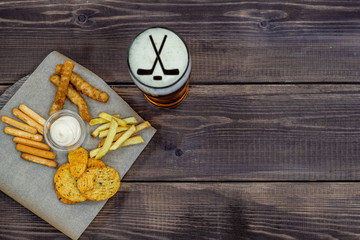Diverse snacks and beer with silhouettes of hockey sticks on dark wooden background. Top view, Empty space for text