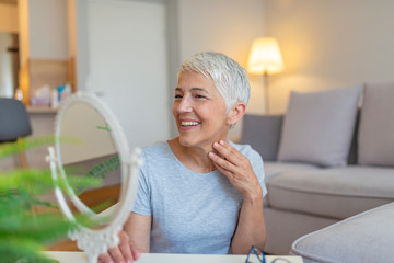 Senior woman touching face in front of mirror, closeup. Portrait of an attractive middle aged woman looking into a mirror. Attractive senior woman looking at herself in mirror