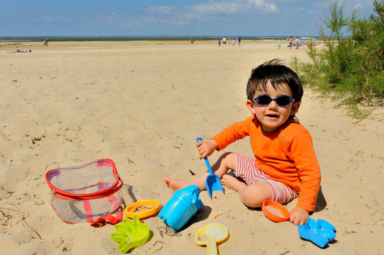 Two-year-old boy playing with his plastic sand moulds on the beach