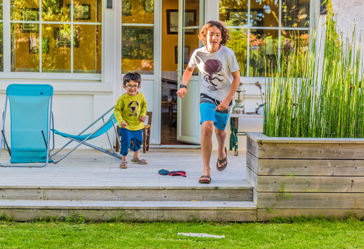 Two boys of five year old and thirteen years old running out of the house towards the garden
