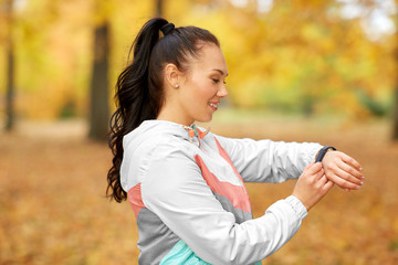 sport, technology and healthy lifestyle concept - young woman looking at fitness tracker in autumn park