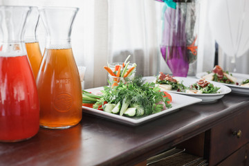 Delicious green salad with fresh vegetables (cucumber, selery, carrot, tomato) in the white dishes on wooden brown table. Fresh lemonade near the dishes.