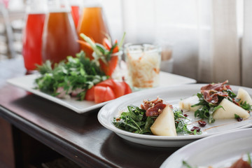 Delicious green salad with fresh vegetables (cucumber, selery, carrot, tomato) in the white dishes on wooden brown table. Fresh lemonade near the dishes.