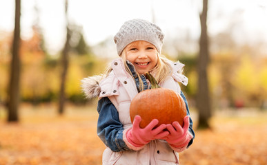 childhood, thanksgiving day and halloween concept - happy little girl with pumpkin at autumn park