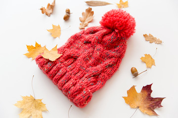 season, headwear and clothes concept - knitted woollen hat and fallen autumn leaves on white...