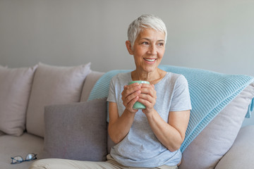  She is enjoying tasty drink while relaxing at living room. Copy space. Shot of a mature woman relaxing at home with a cup of coffee while sitting on sofa