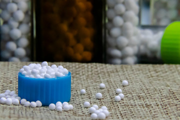 Close image of Homeopathic granules in small bottle cap and some pills scattered on the jute sack surface with blurred white sugar ball medicine bottles.