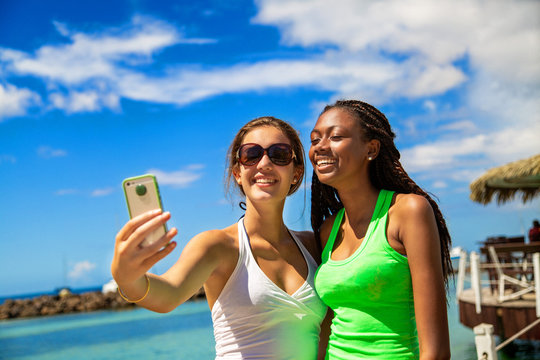 2 smiling girls taking a selfie against blue sky background.