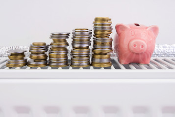 Piggy bank with coins on the heater at home. Conceptual image of the high cost of heating, saving money, saving energy, energy efficiency.