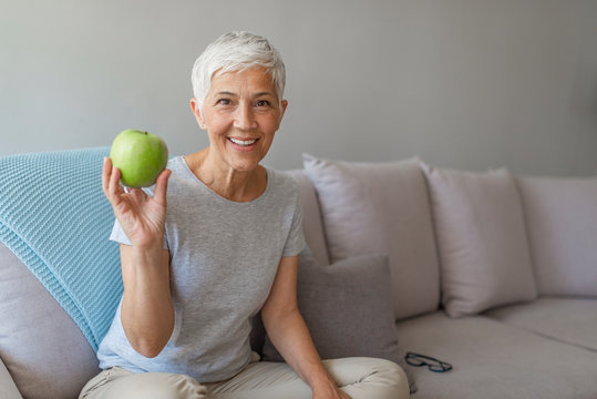 Older Woman With Healthy Food Indoors. Happy Senior Woman With Green Apple At Home. Senior Woman Holding An Apple. Age, Healthy Eating, Food, Diet And People Concept