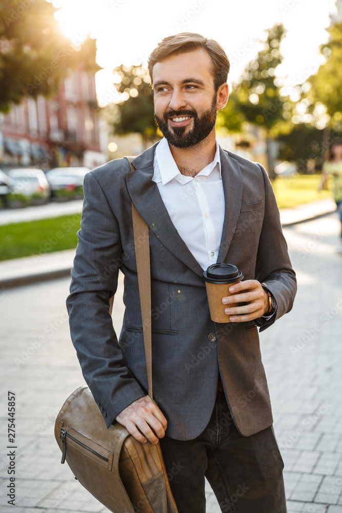 Poster portrait of caucasian adult businessman in formal suit holding takeaway coffee while walking through